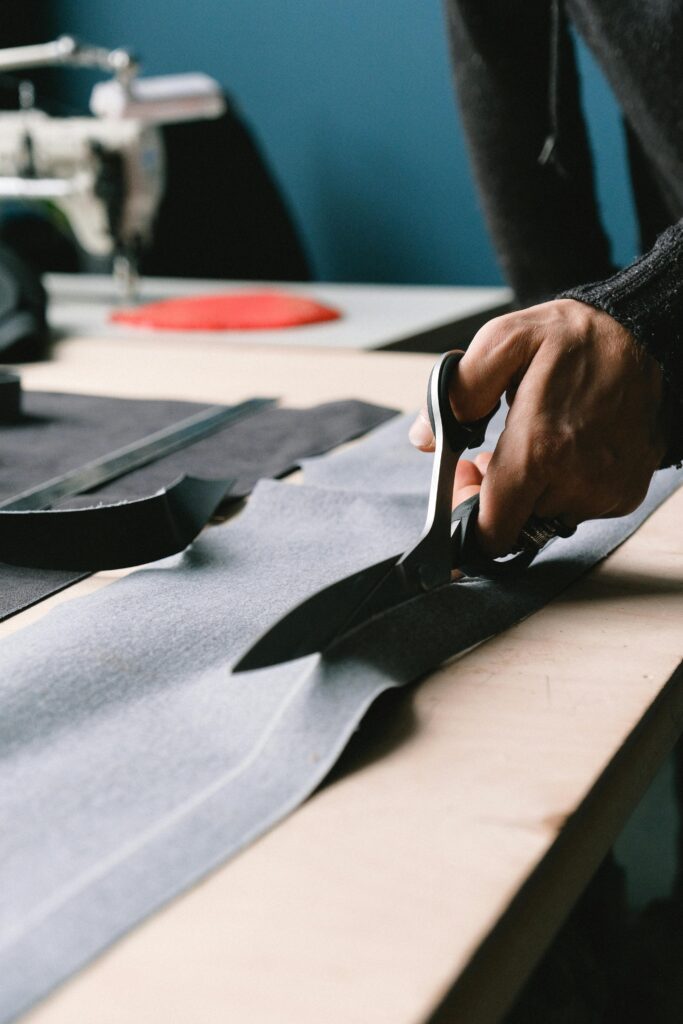 A tailor precisely cuts fabric on a workbench with professional scissors.